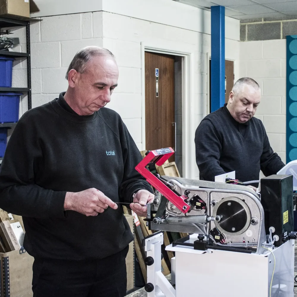 Two employees at Total PFS working on servicing printing machines at a workbench